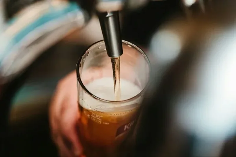 Cerveja sendo servida em copo de vidro com espuma, em ambiente de bar associado a momentos de lazer e futebol. Foto de BENCE BOROS na Unsplash 
